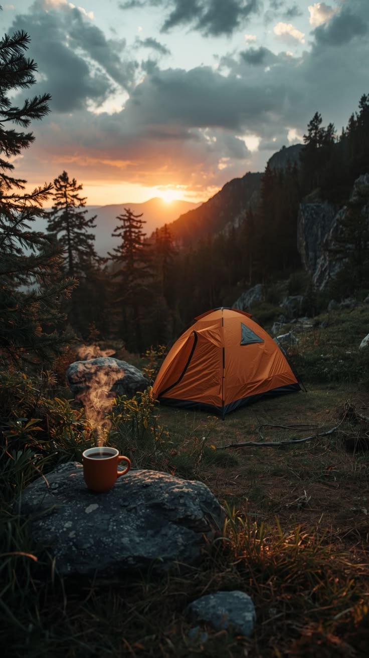 Orange dome tent on a grassy slope at sunrise, with a steaming mug on a rock in the foreground